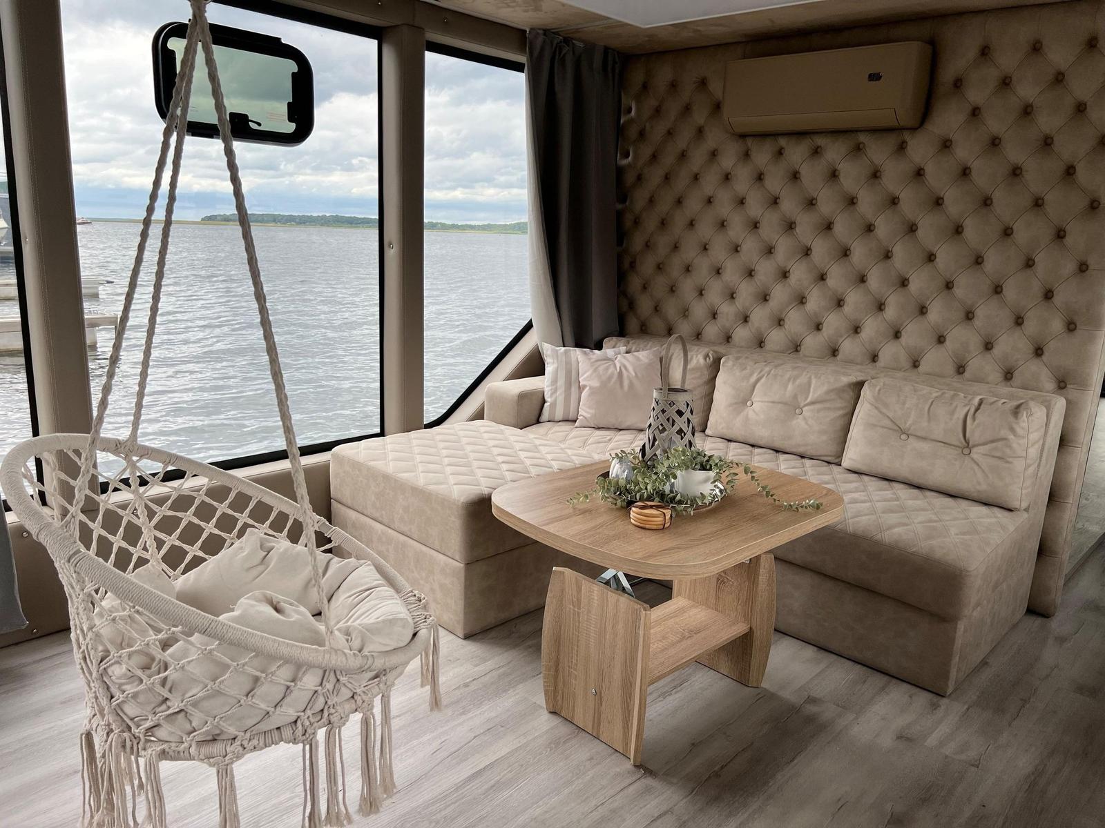 Wohnbereich mit Sofa, Hängesessel und Blick auf Wasser.