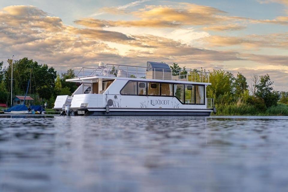 Ein weißes Hausboot mit Balkon liegt auf ruhigem Wasser bei Sonnenuntergang.