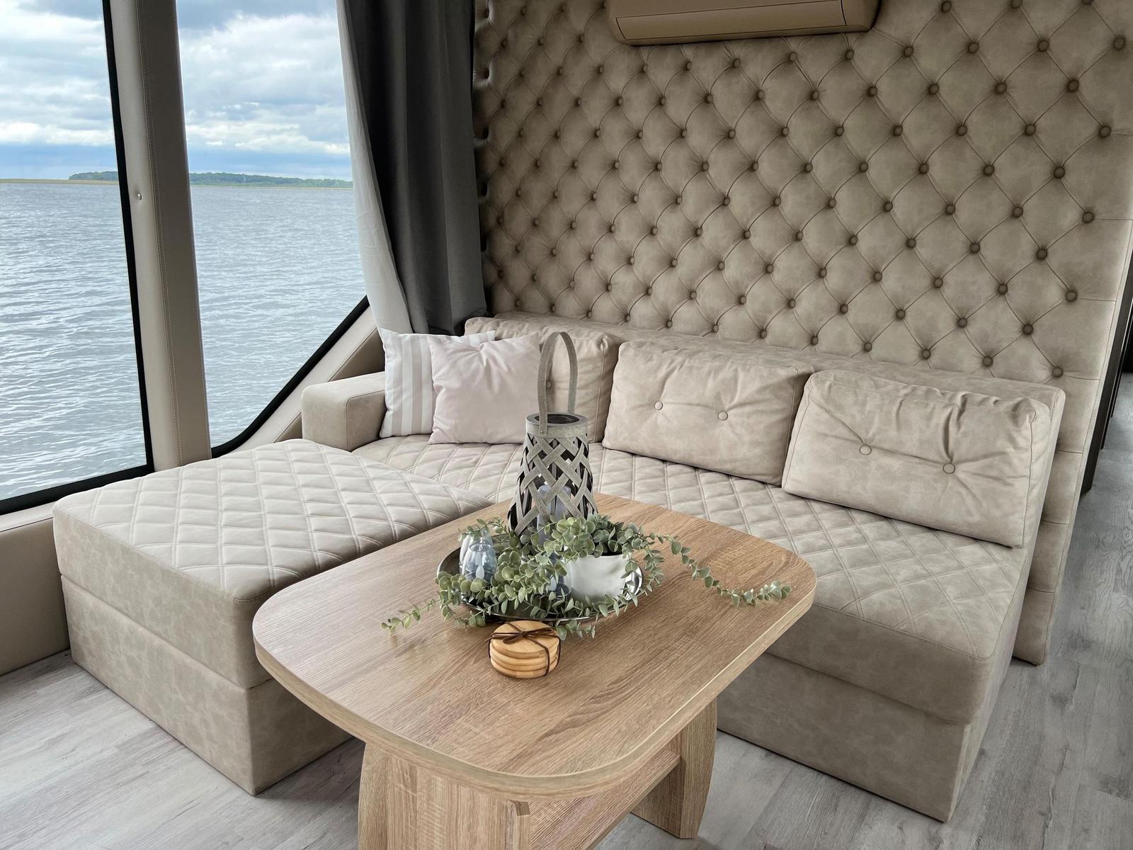 Sofa mit Hocker und Tisch vor großem Fenster mit Blick auf Wasser.