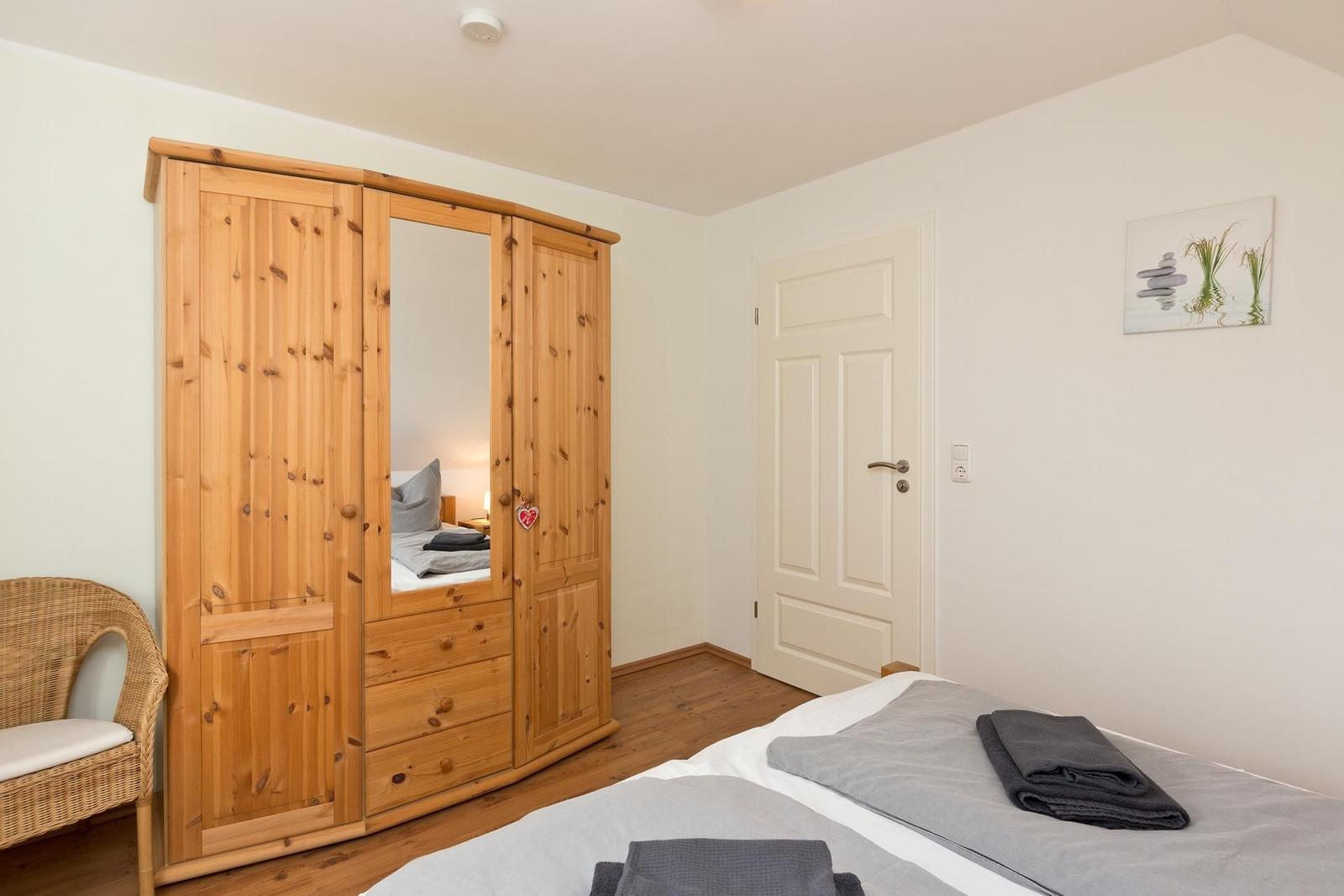 Schlafzimmer mit Holzschrank, Bett und Stuhl. Wandbild und Tür sind sichtbar.