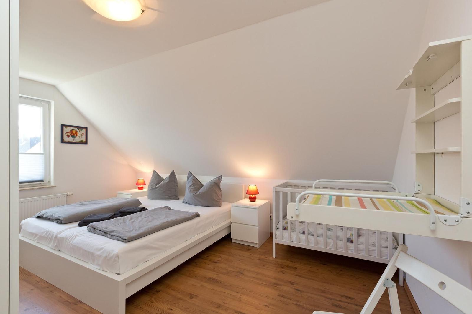 Zimmer mit Doppelbett, Kinderbett und Schrank an der Wand.