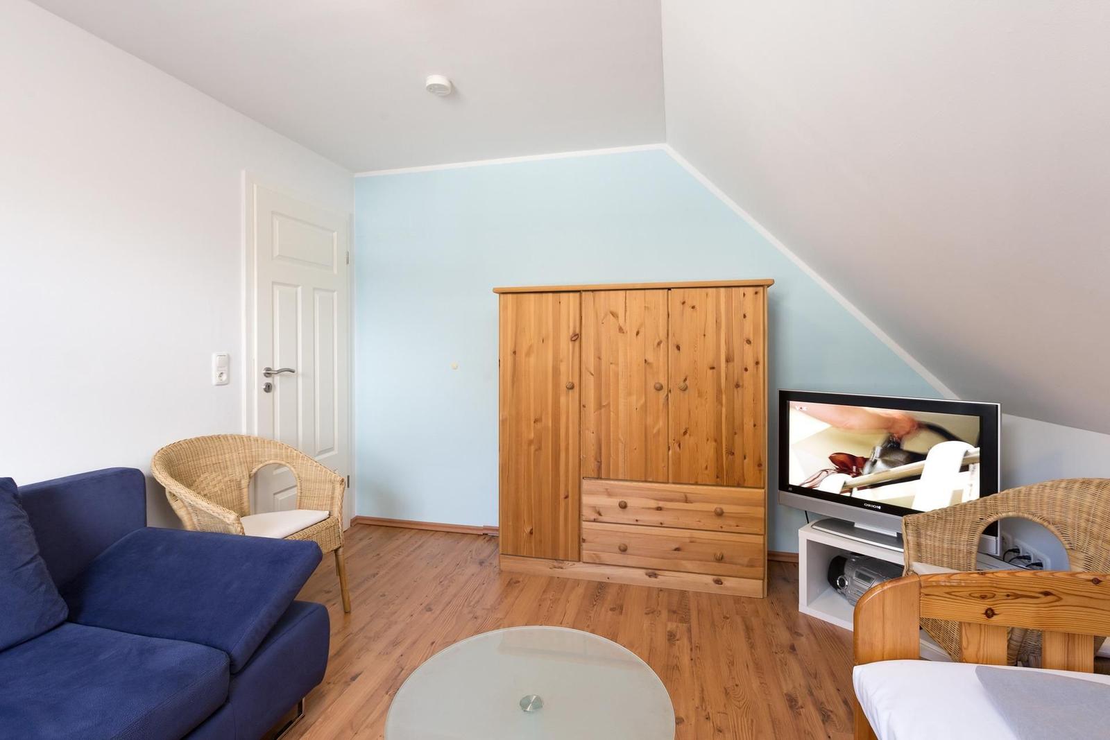 Ein Raum mit blauer Wand, Holzmöbeln und einem Sofa. Fernseher und Rattanstühle sind vorhanden.