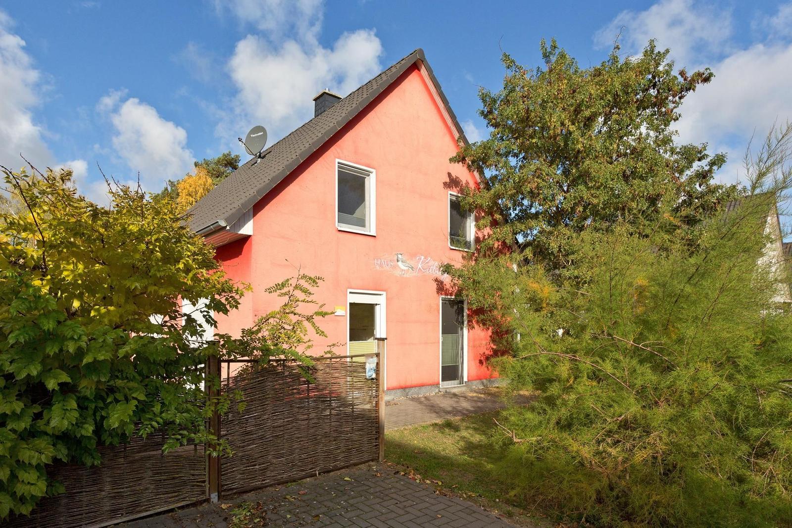 Rotes Haus mit Gartenzaun und Bäumen unter blauem Himmel.