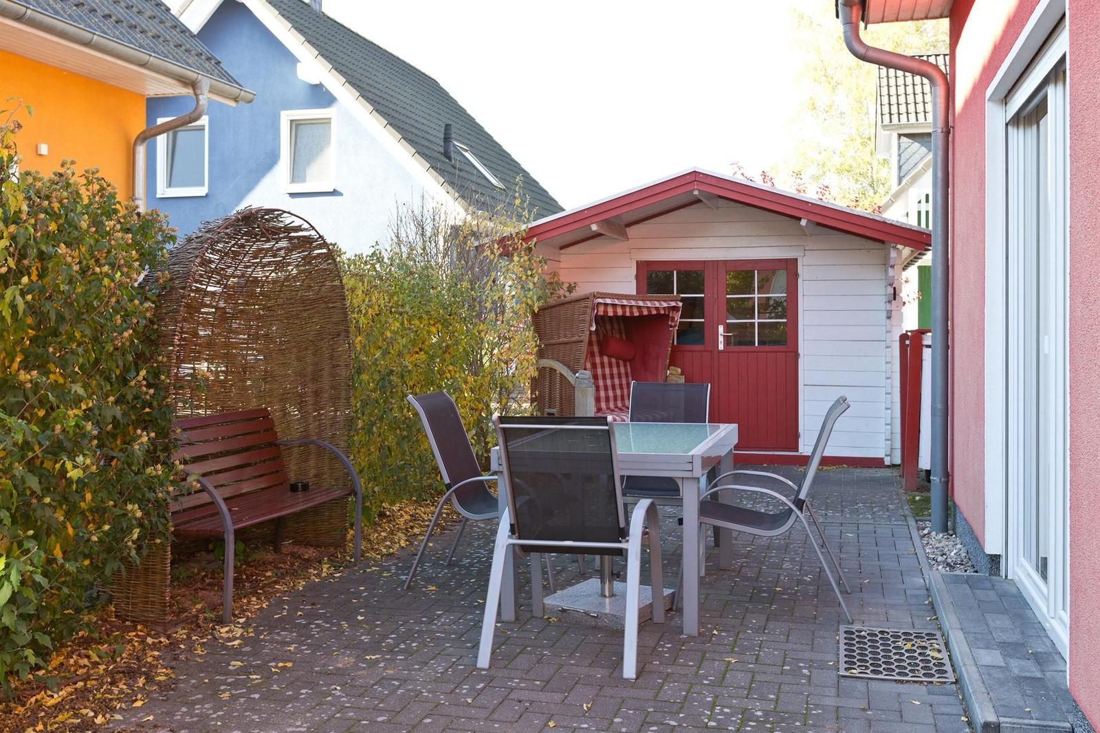 Terrasse mit Tisch, Stühlen, Wickerbank und kleinem Holzhaus.