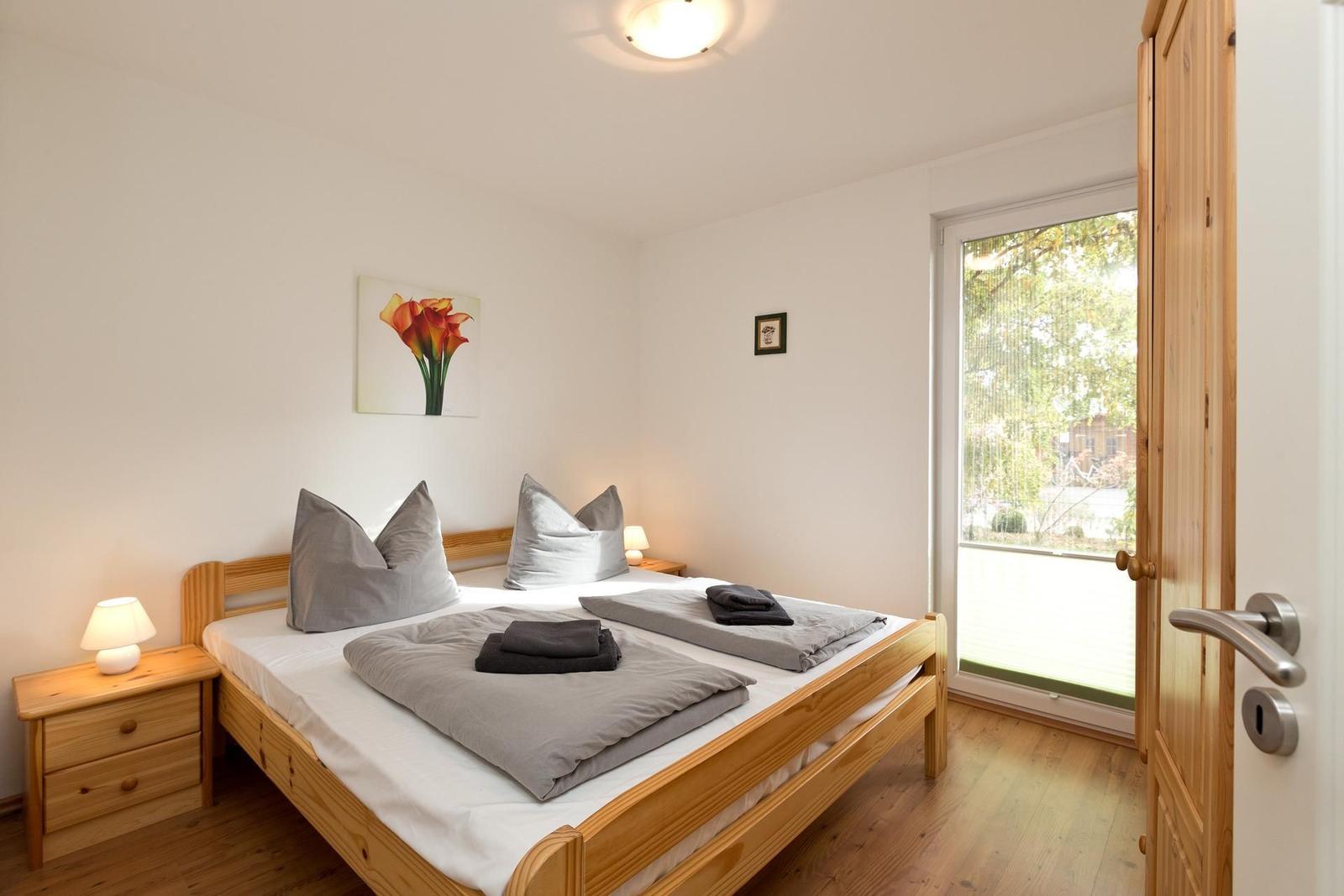 Schlafzimmer mit Holzbett, Nachttisch und Fenster. Wandbild und Holztür sichtbar.
