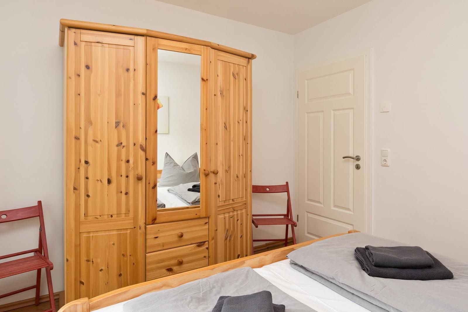 Schlafzimmer mit Holzschrank, Bett und zwei roten Stühlen.