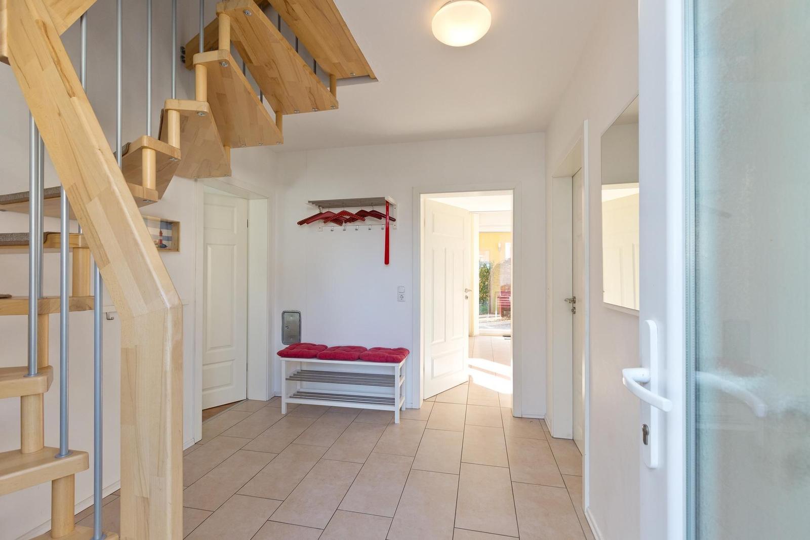 Hausflur mit Holztreppe, roter Sitzbank und Garderobe.