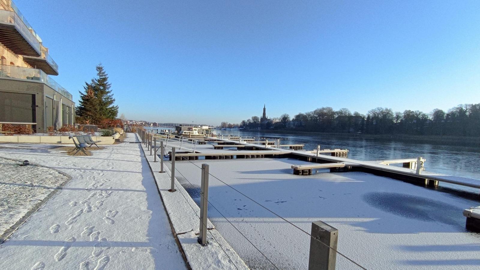 Schneebedeckter Bootssteg am Fluss mit Blick auf die Stadt