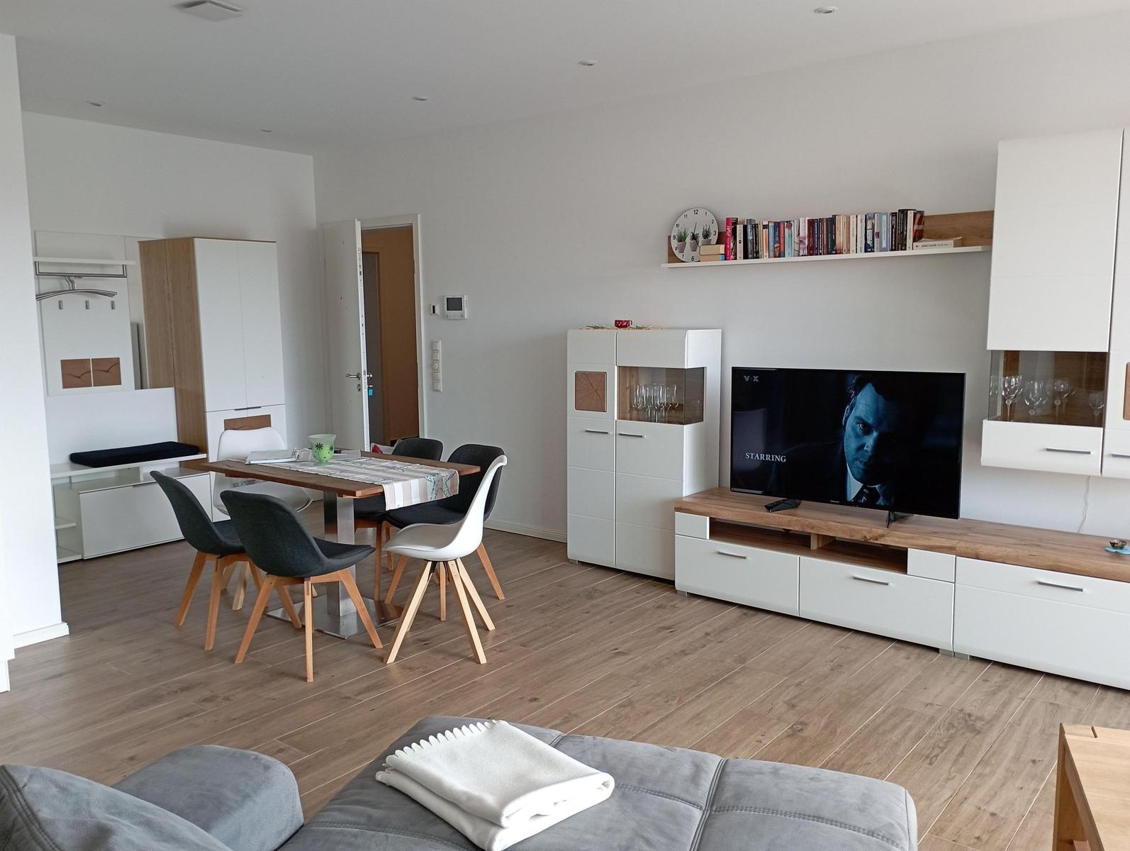 Wohn- und Essbereich mit TV, Tisch und Stühlen sowie Schränken und Holzboden.