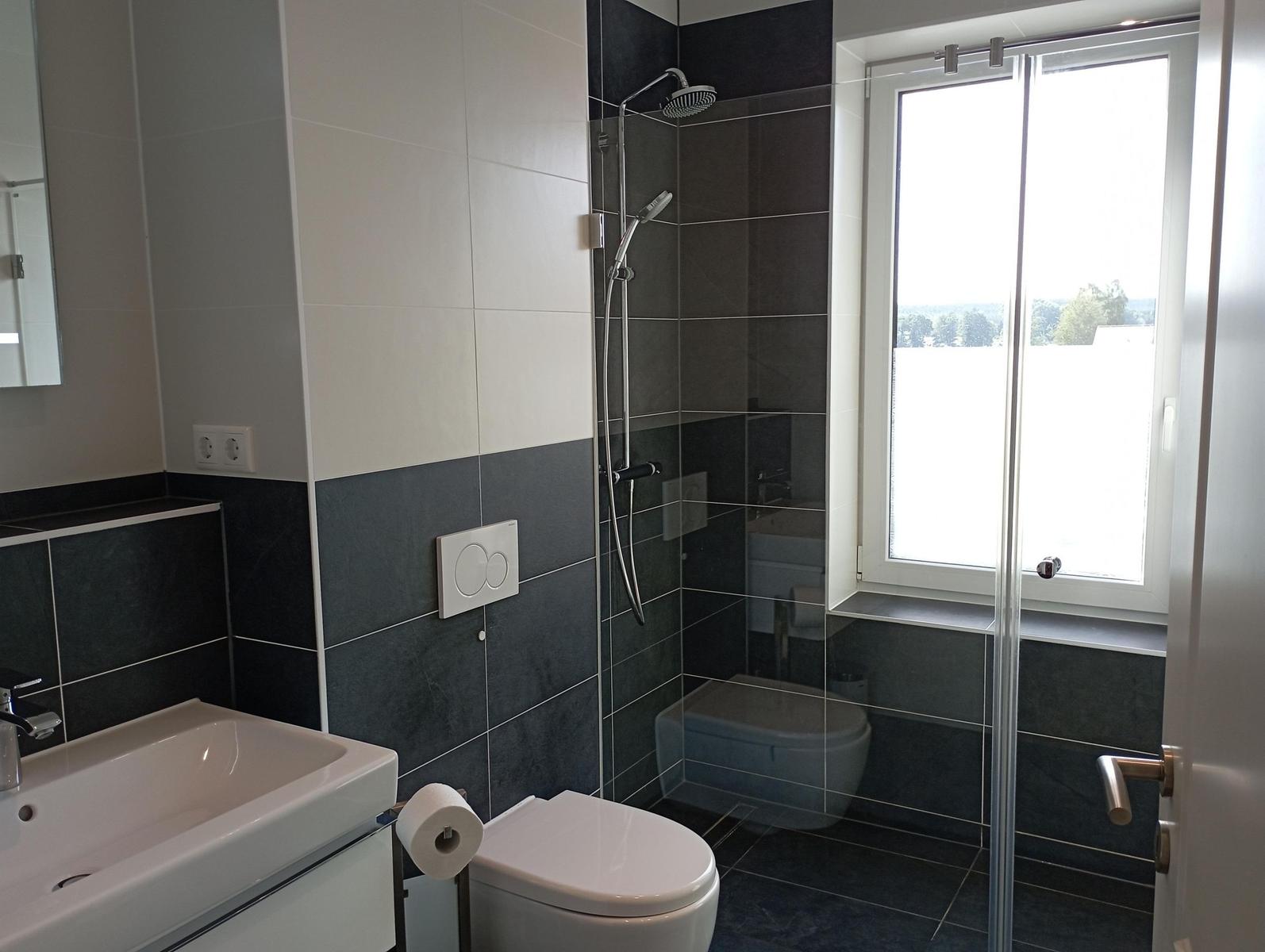 Badezimmer mit Dusche, Toilette und Waschbecken. Fenster mit Blick nach draußen.