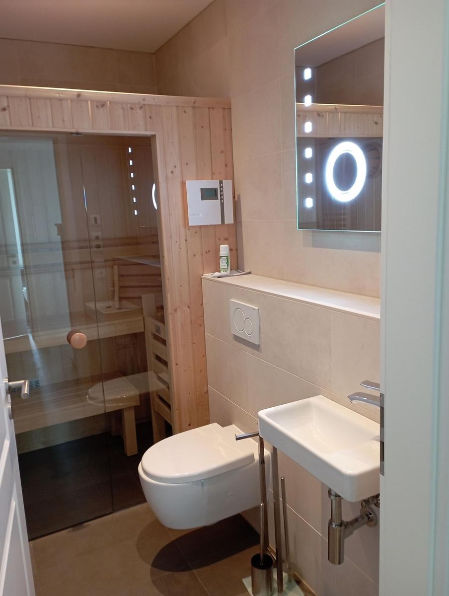 Badezimmer mit Dusche, Toilette und Waschbecken. Spiegel mit Beleuchtung.