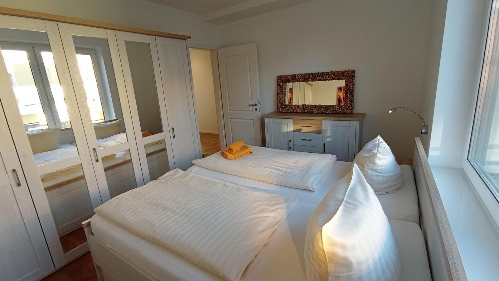 Zimmer mit Doppelbett, Kleiderschrank und Schminktisch mit Spiegel.