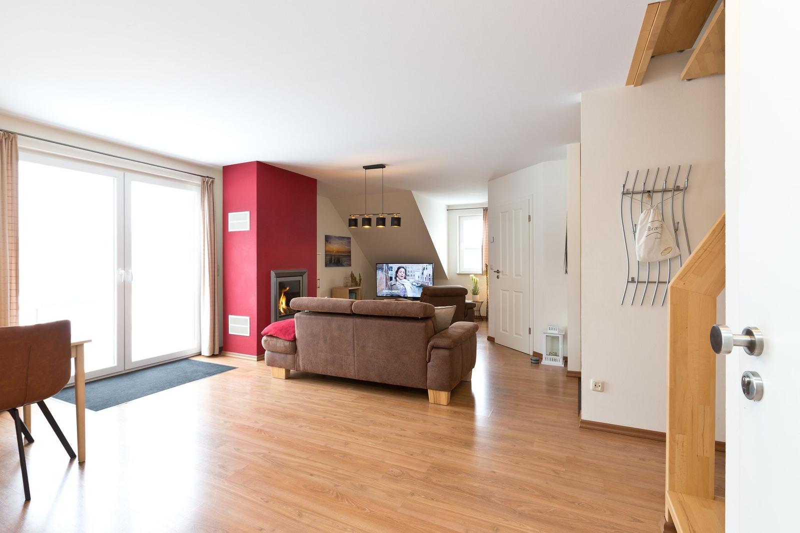 Wohnzimmer mit Sofa, Kamin und TV. Holzboden und große Glastüren.