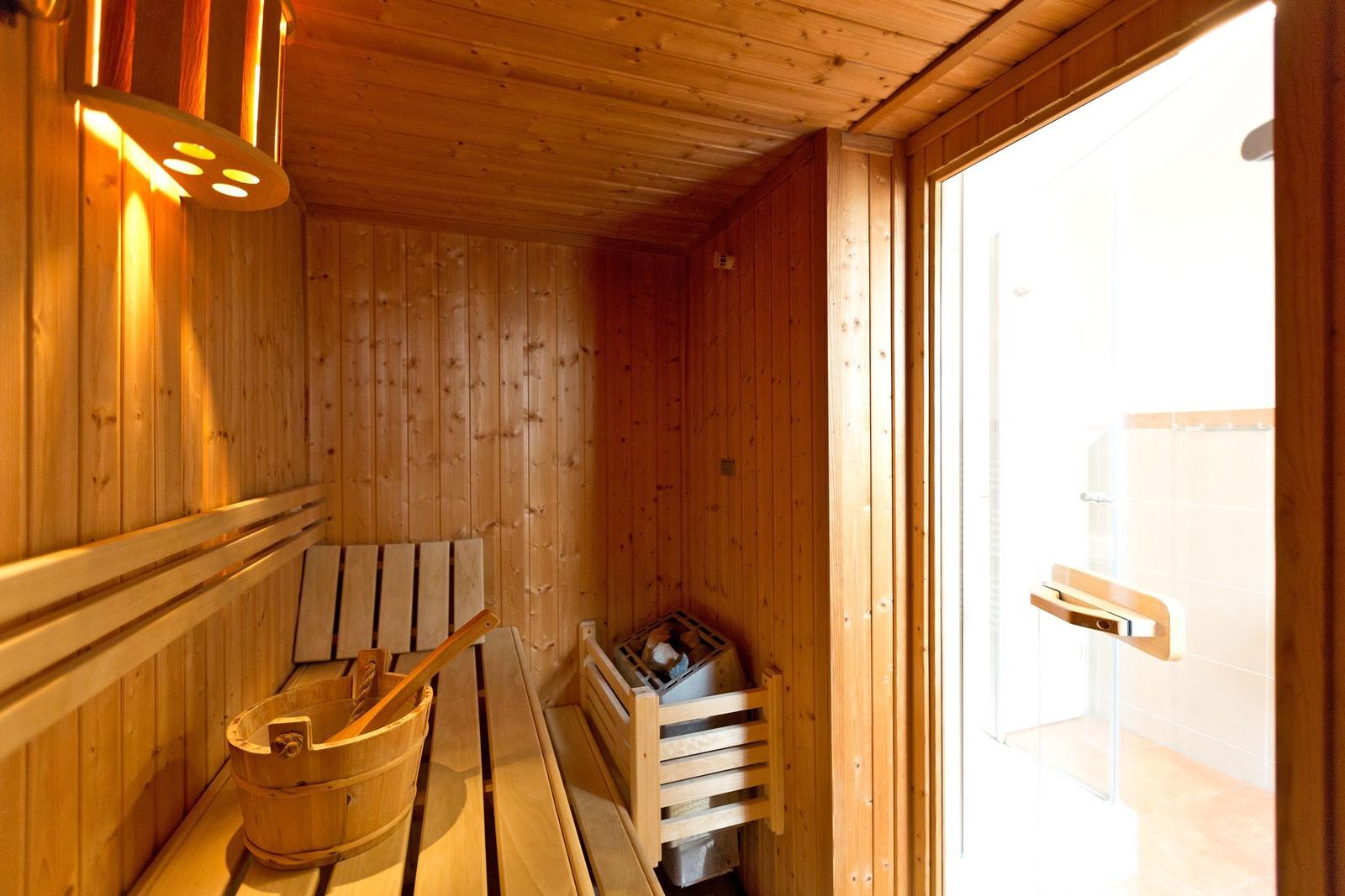 Sauna mit Holzbank, Eimer und Heizung. Tür führt in Dusche.