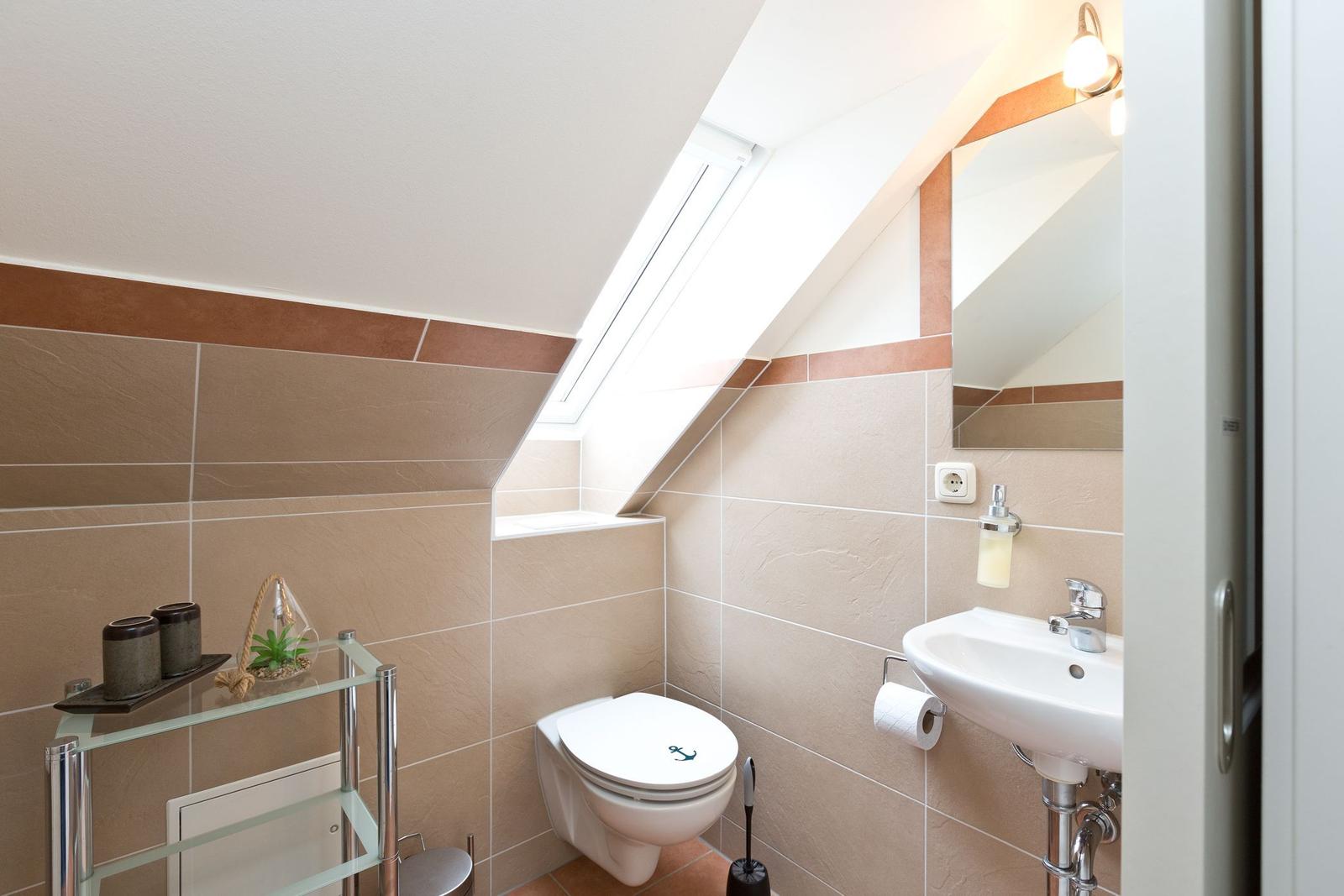 Badezimmer mit Toilette, Waschbecken und Dachfenster. Wandfliesen und Spiegel sichtbar.
