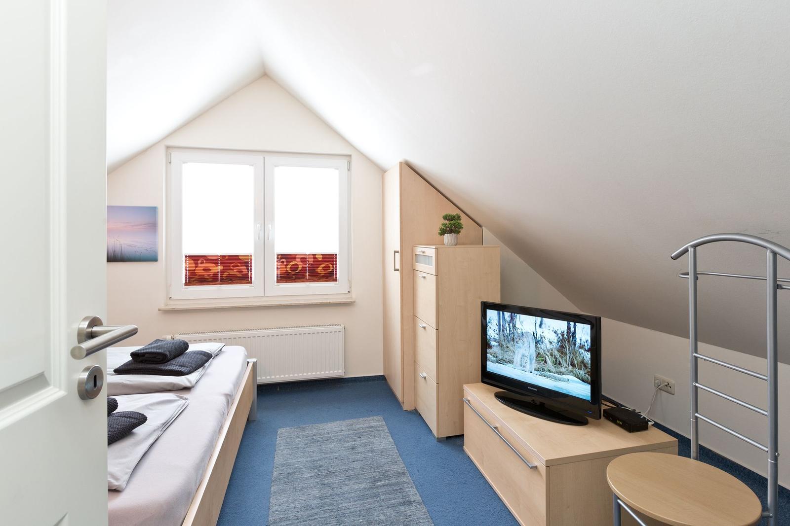 Schlafzimmer mit Bett, TV und Kleiderschrank unter Dachschrägen.
