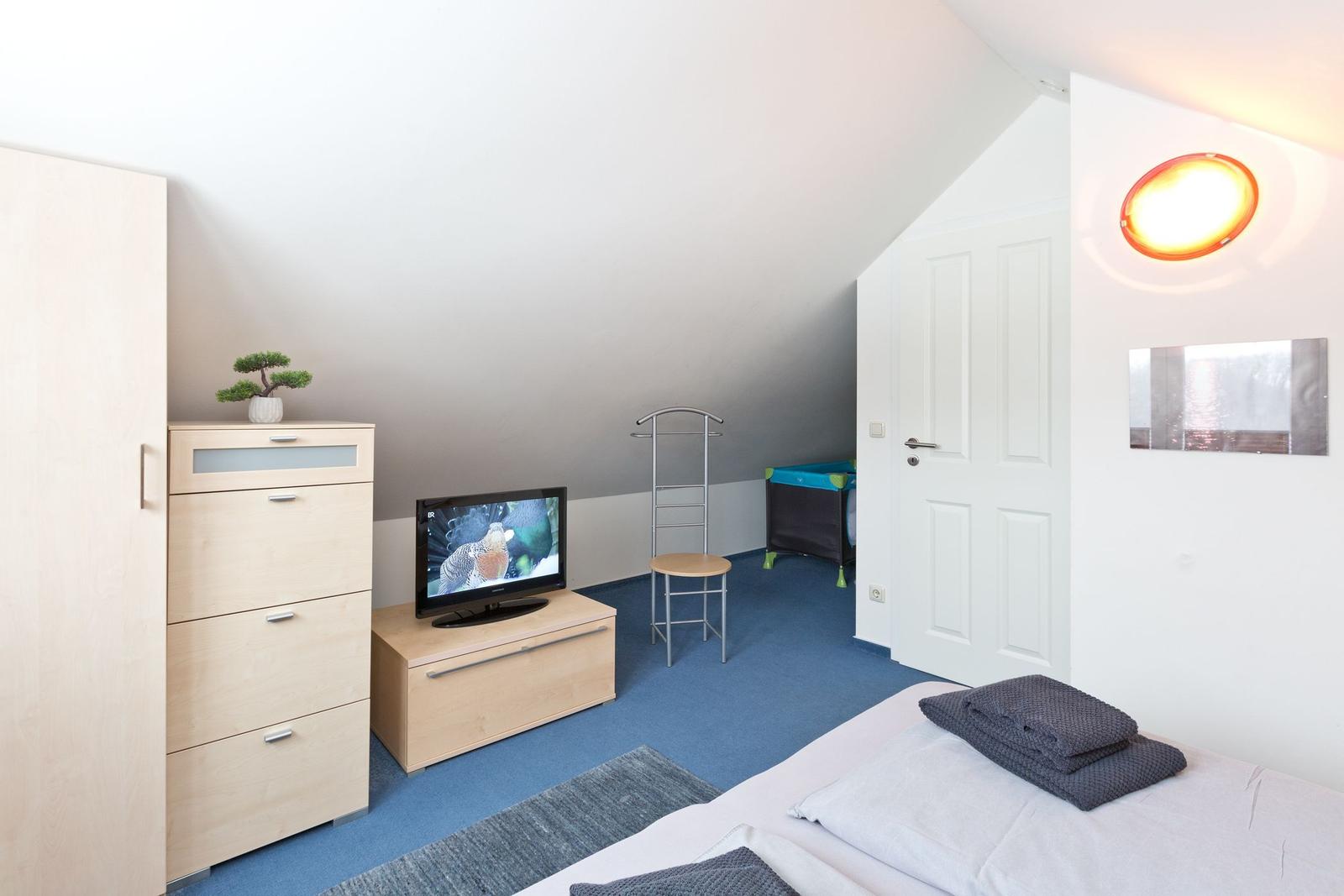 Schlafzimmer mit Bett, TV, Schrank und Kinderbett unter Dachschrägen.