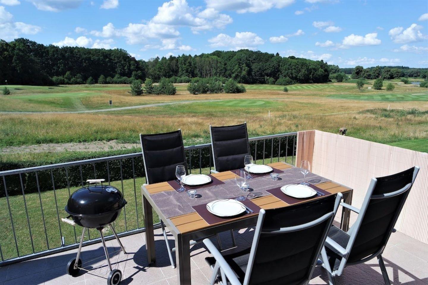 Terrasse mit Tisch, Stühlen und Grill. Blick auf Golfplatz und Wald.