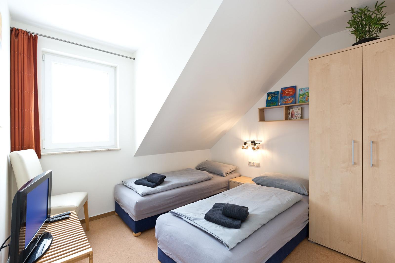 Zwei Betten, Schrank, TV und Fenster mit Vorhang in einem Dachzimmer.