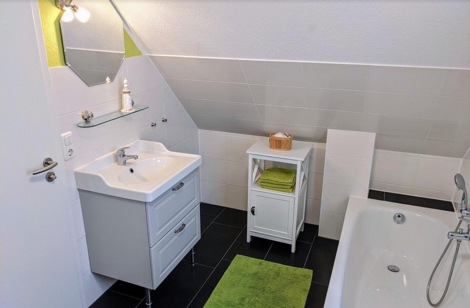 Badezimmer mit Waschbecken, Badewanne und grünen Handtüchern.