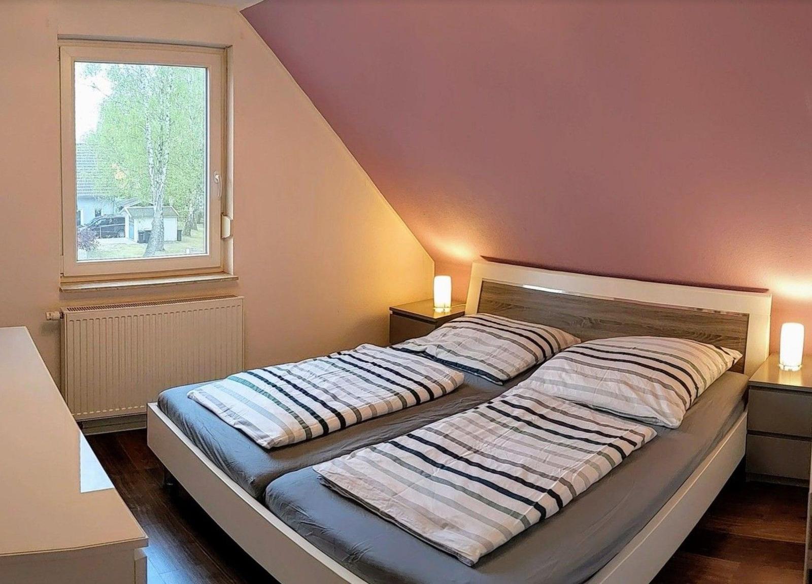 Schlafzimmer mit Doppelbett, Fenster und Nachttischen mit Lampen.