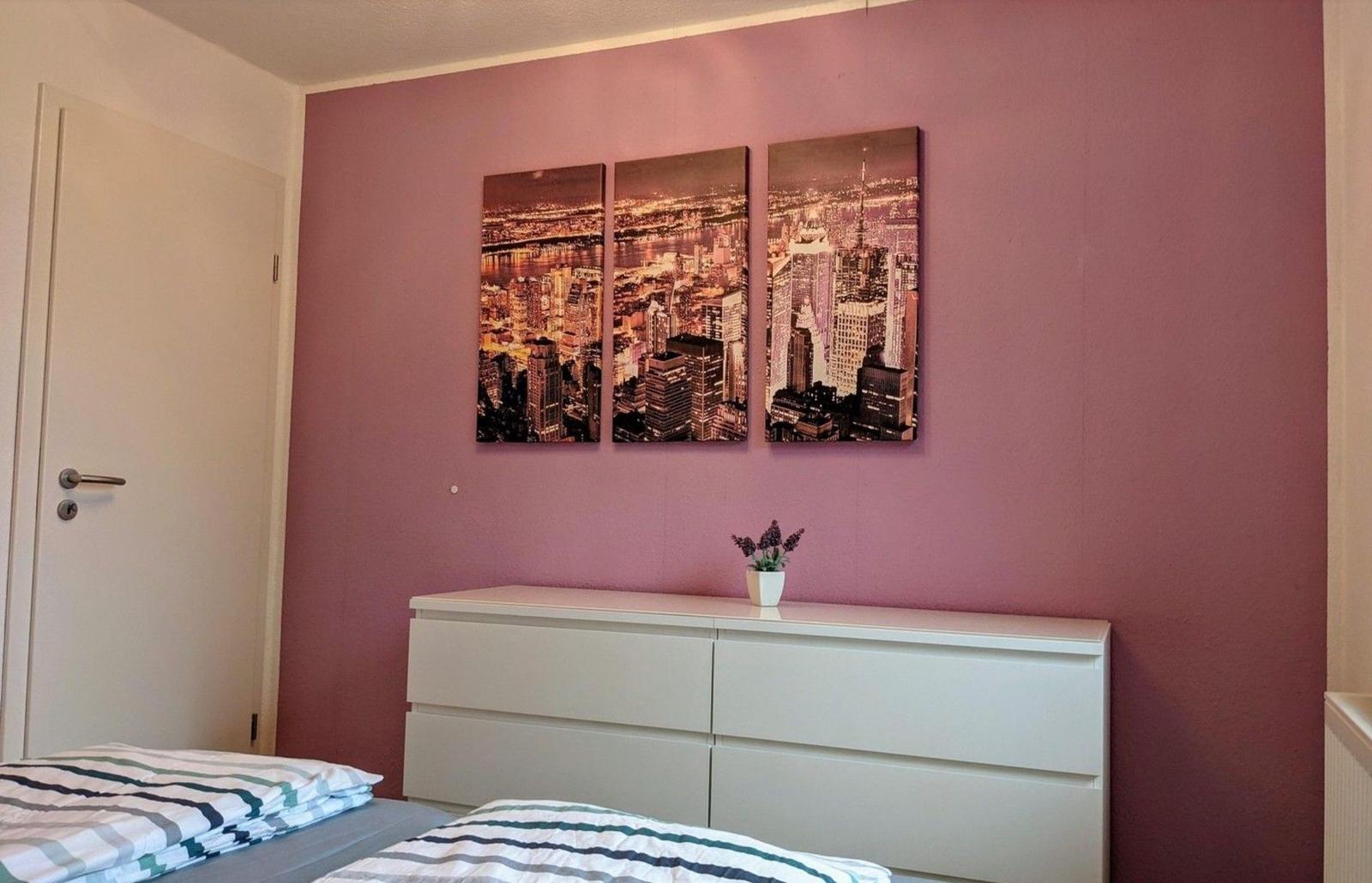 Schlafzimmer mit rosa Wand, weißem Schrank und dreiteiliger Stadtansicht