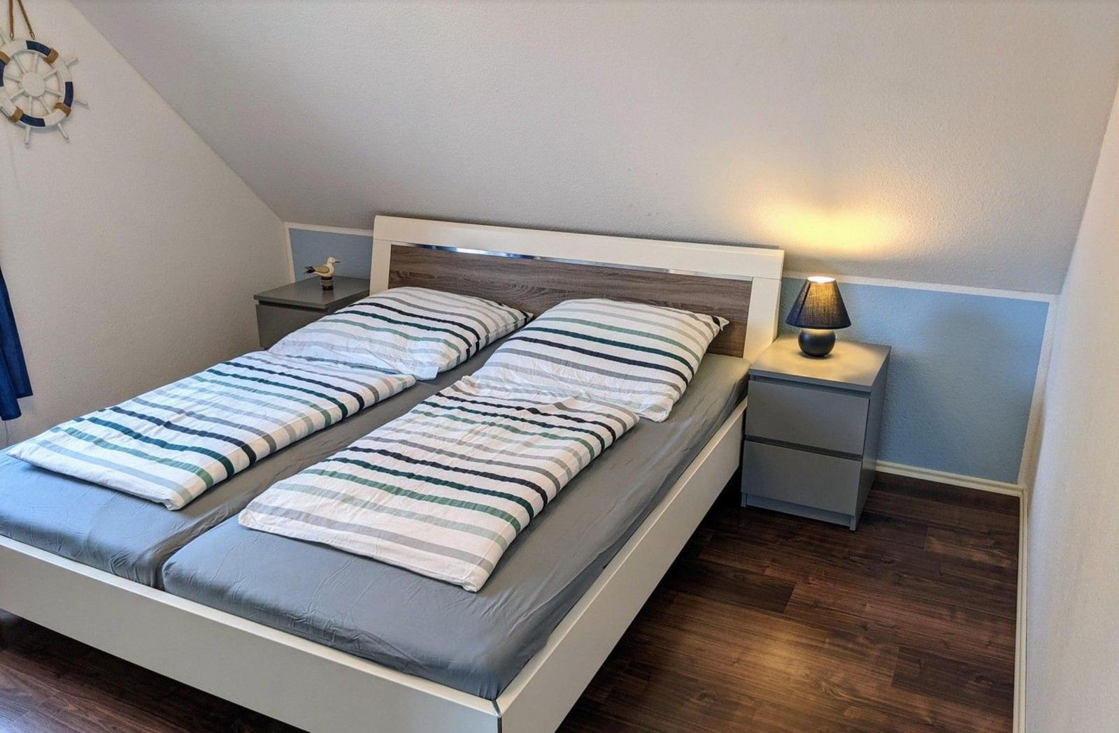 Schlafzimmer mit Doppelbett, Nachttisch und Lampe. Holzfußboden und schräger Dachfirst.