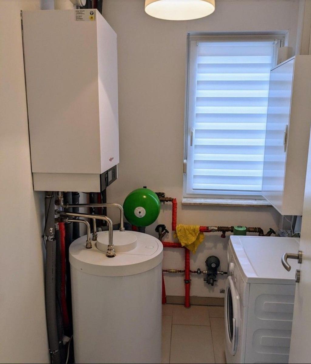 Heizungsraum mit Boiler, Waschmaschine und Fenster mit Jalousie.