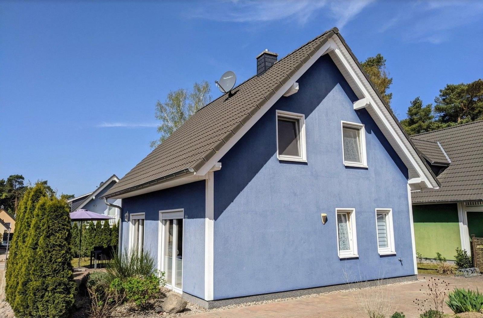 Blau gestrichenes Einfamilienhaus mit Dachterrasse und Gartenbereich unter klarem Himmel.