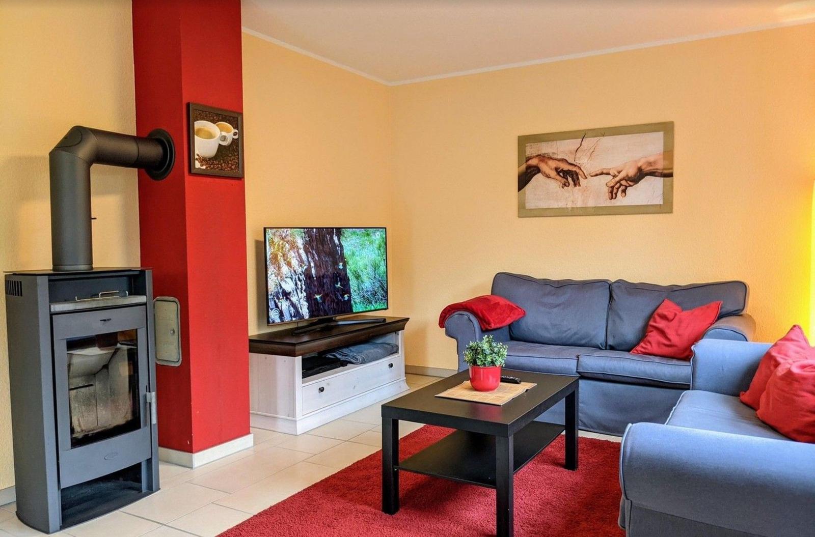 Wohnzimmer mit Sofa, Fernseher und Kaminofen. Wandbild und roter Teppich.