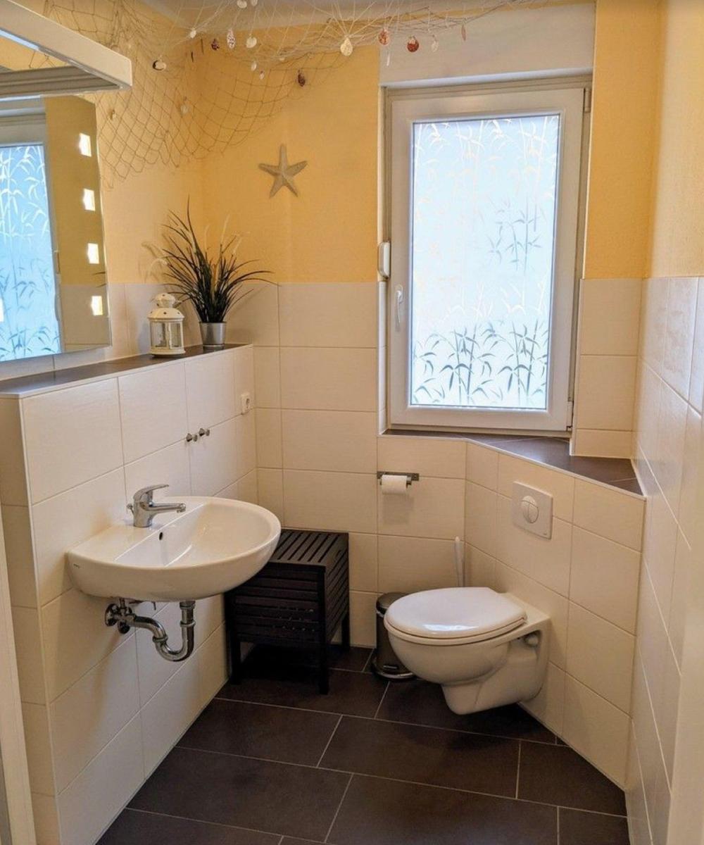 Badezimmer mit Waschbecken, Toilette und Fenster mit Bambusmuster.