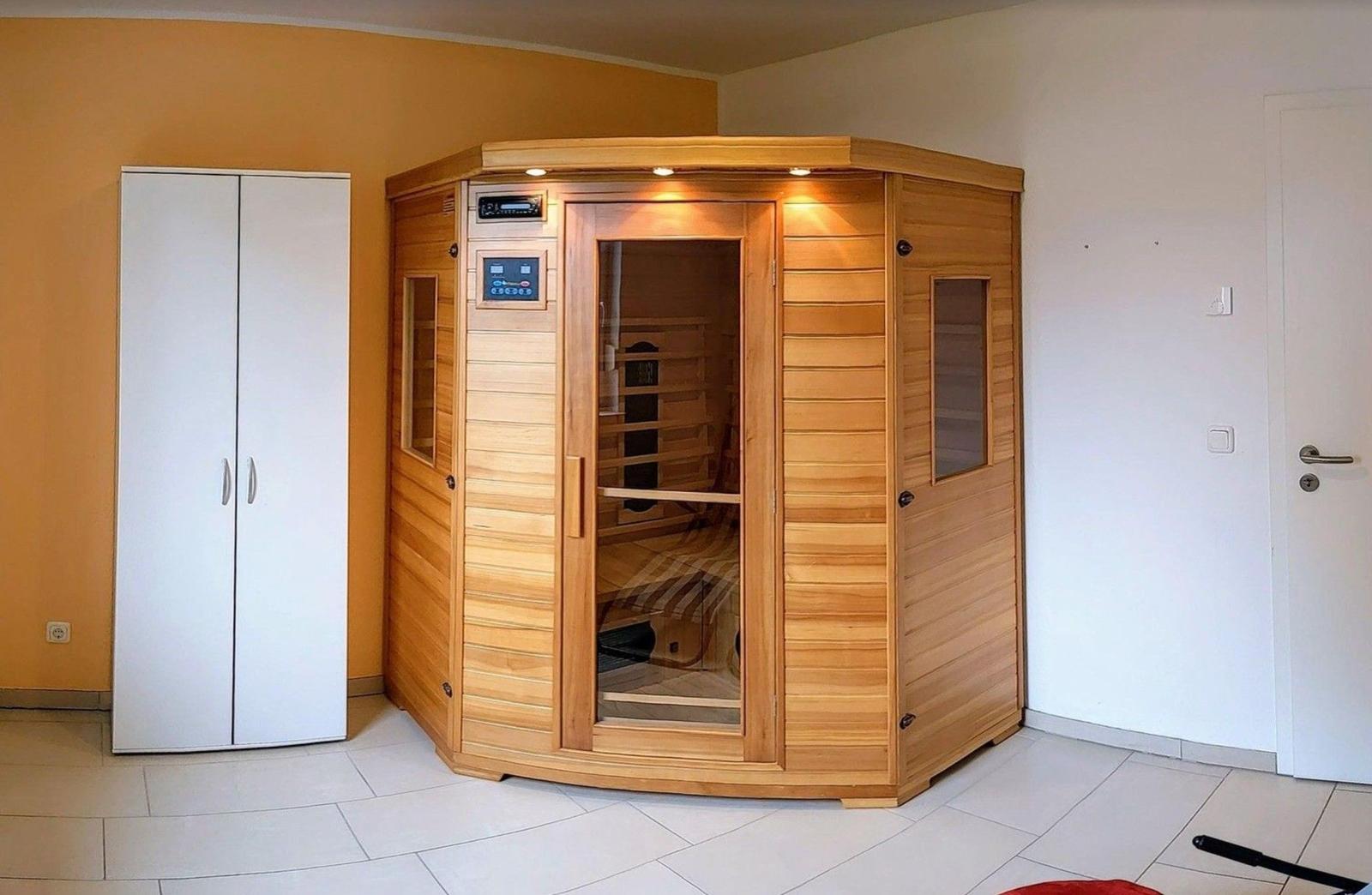 Holz-Infrarot-Sauna mit Glasfront und Bedienfeld. Weiße Schrankwand und weiße Tür im Hintergrund.