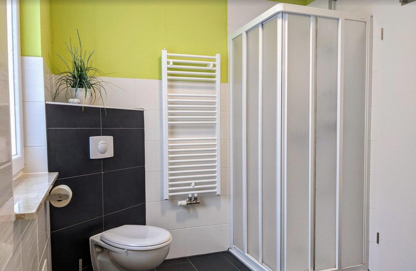 Badezimmer mit Dusche, Toilette und Heizkörper an der Wand.