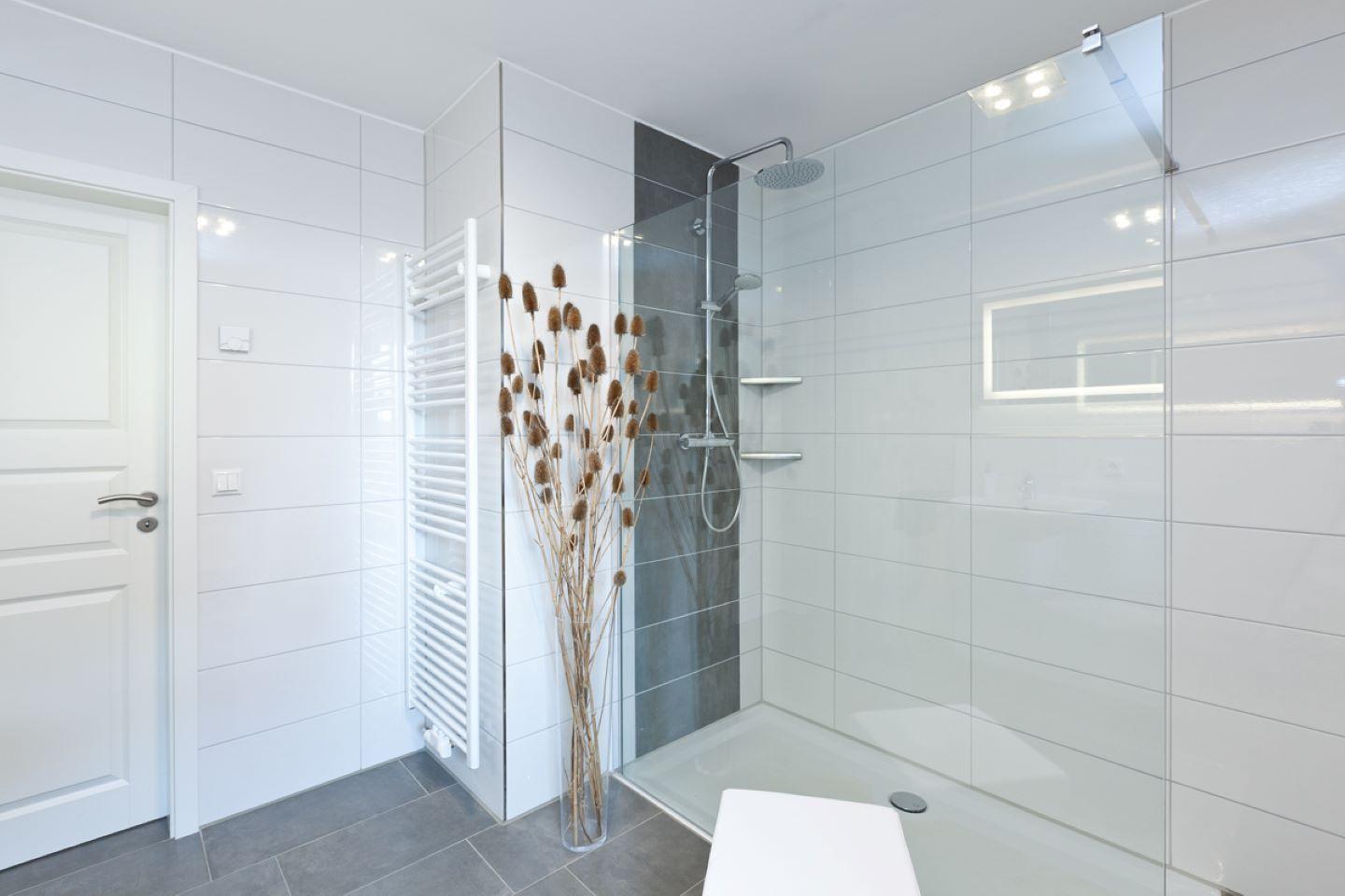 Moderne Dusche mit Glaswand, weiße Fliesen und Holzdekoration.