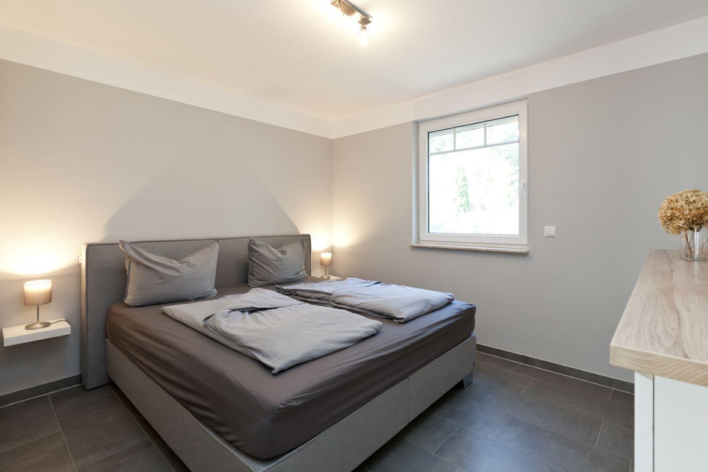Schlafzimmer mit Doppelbett, Fenster und Nachttisch mit Lampe.