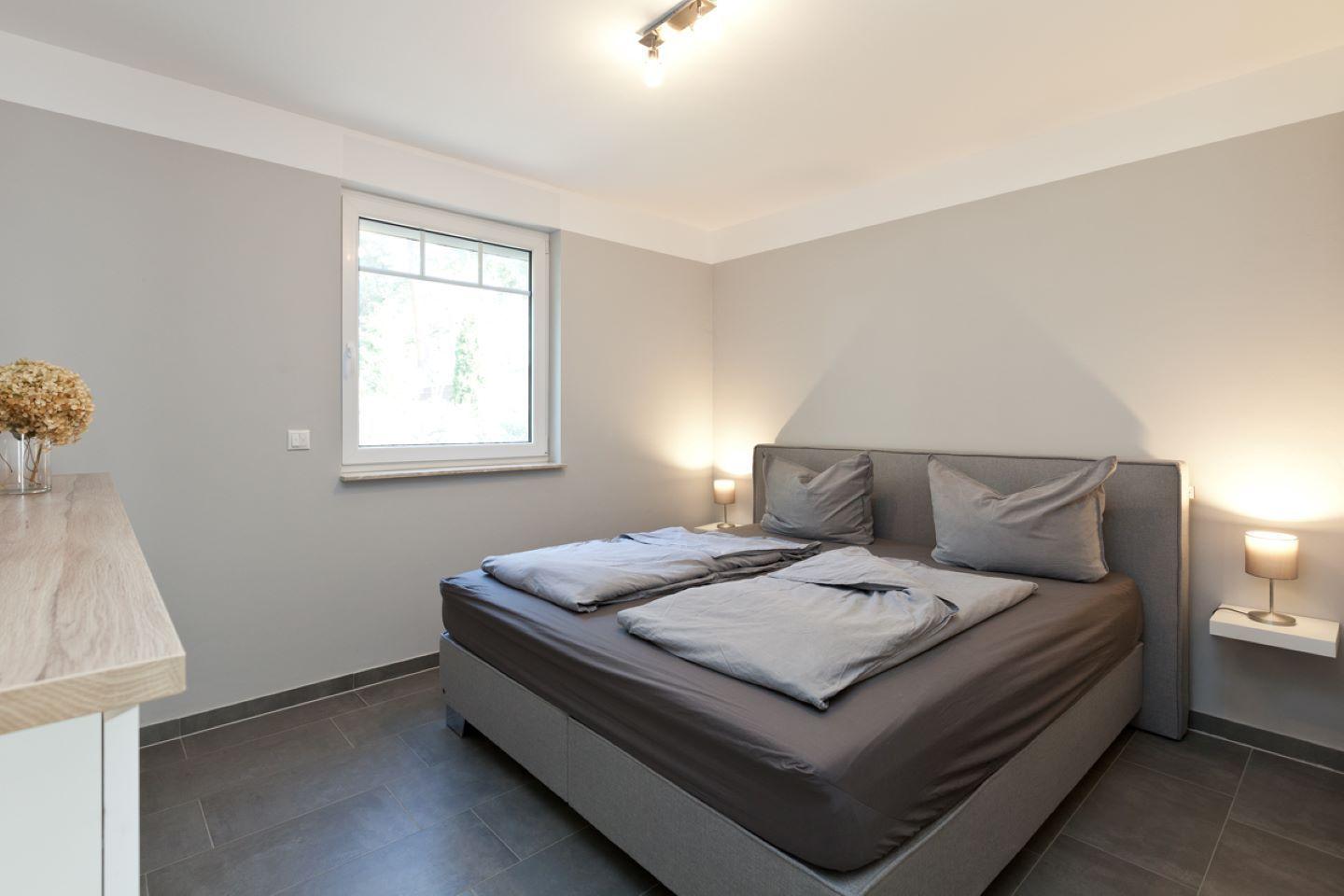 Schlafzimmer mit Doppelbett, Fenster und Nachttischen mit Lampen.