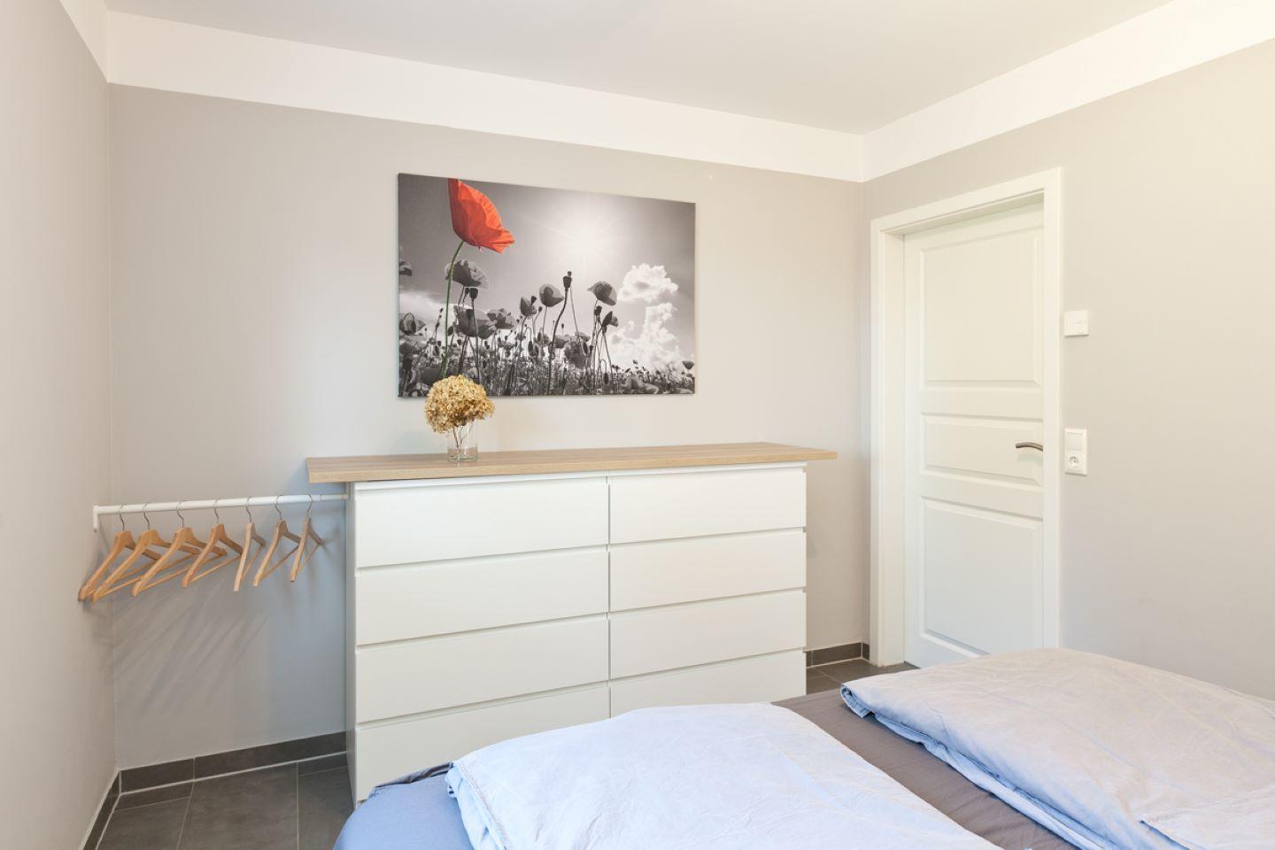 Schlafzimmer mit weißem Schrank, Bett und Wandbild mit Mohnblume.