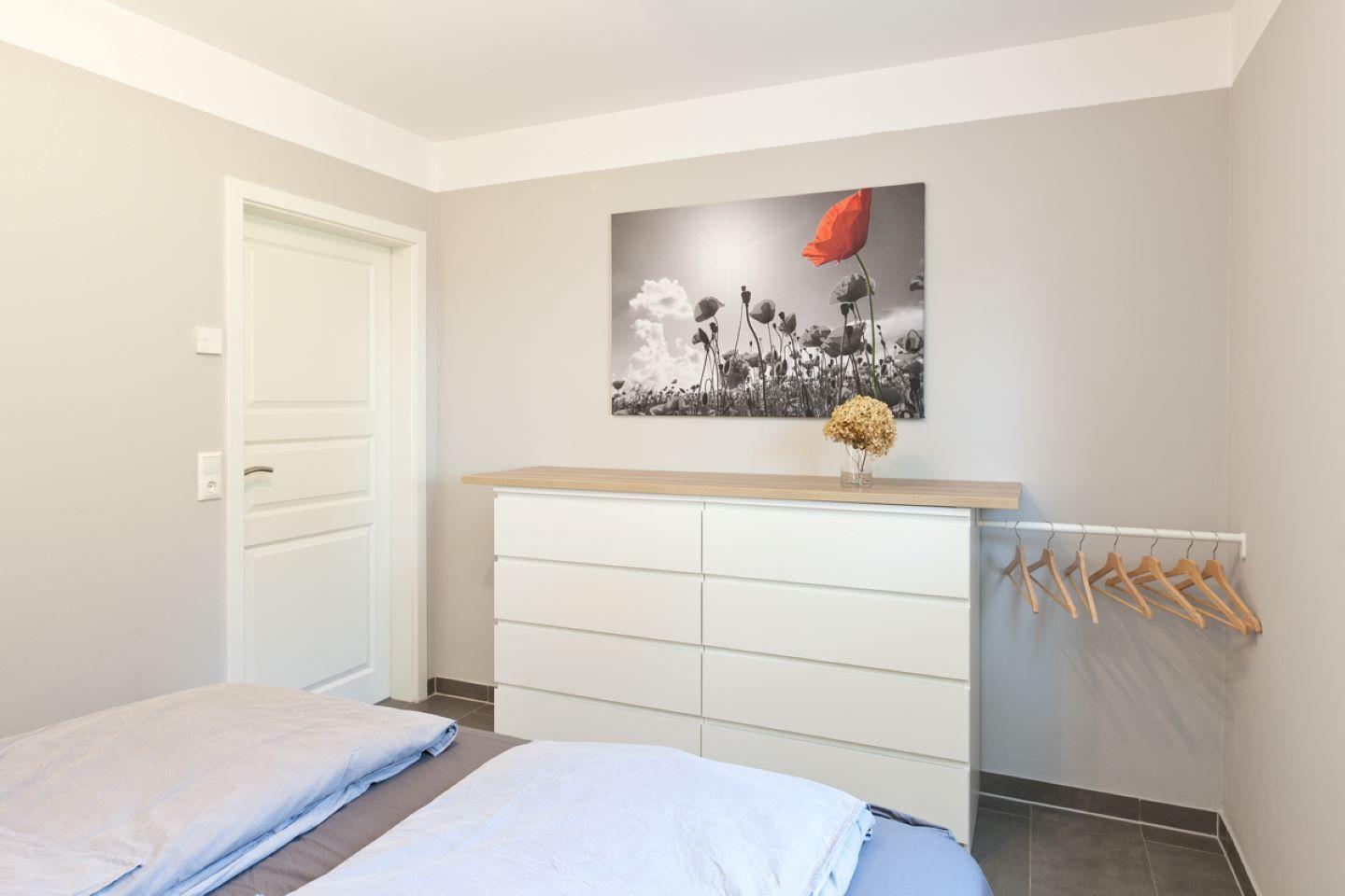Schlafzimmer mit Bett, Kleiderschrank und Wandbild mit Mohnblume.