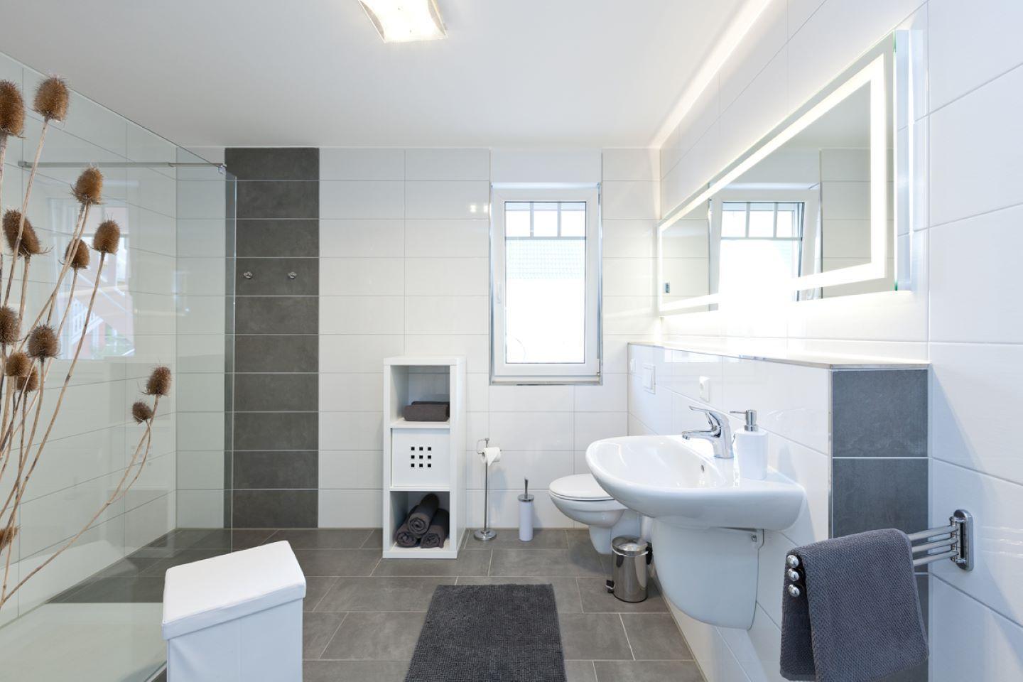 Badezimmer mit Dusche, Waschbecken und Toilette. Graue Fliesen und weißer Einbau.