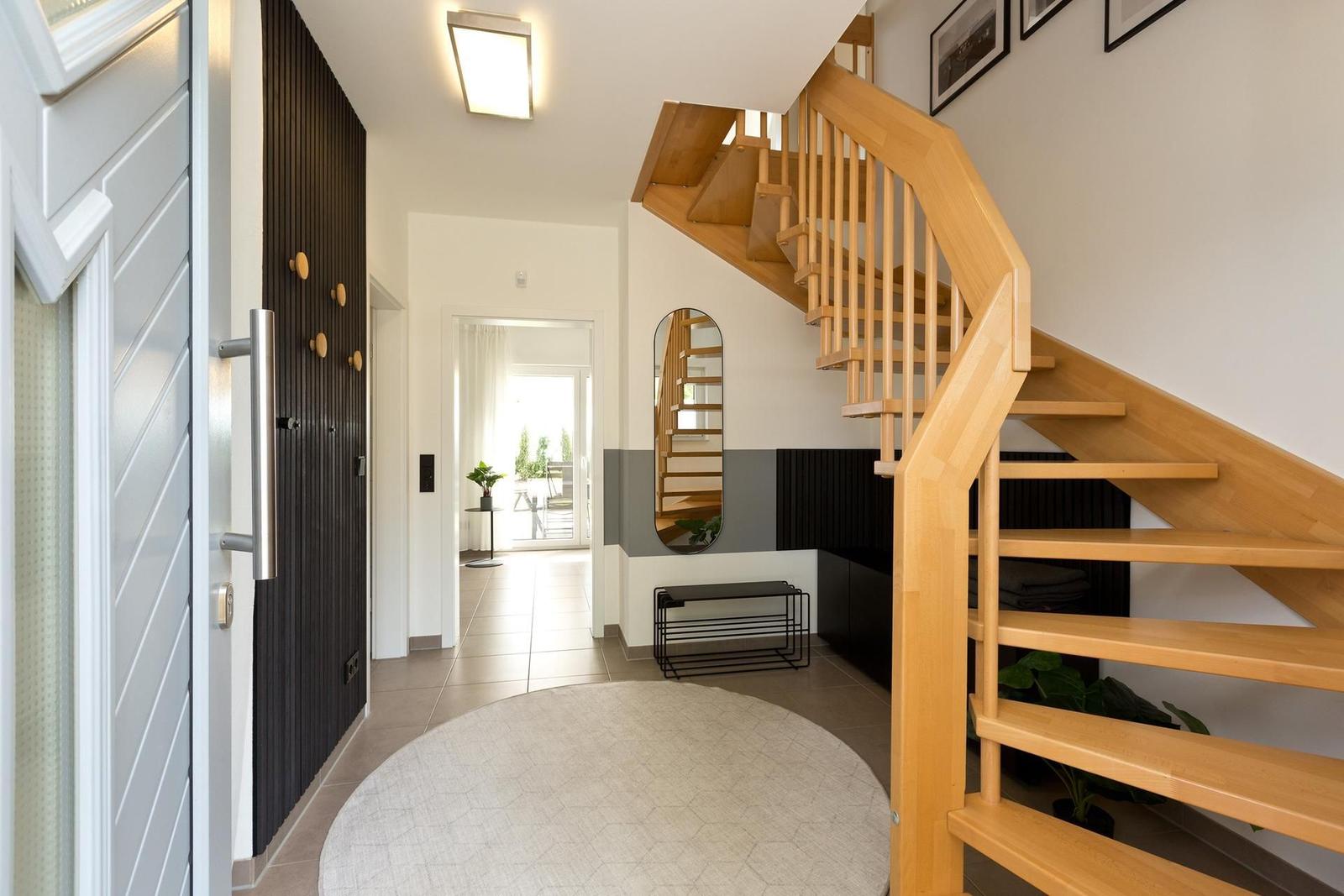 Eingangsbereich mit Holztreppe, runder Teppich und Spiegel an der Wand.