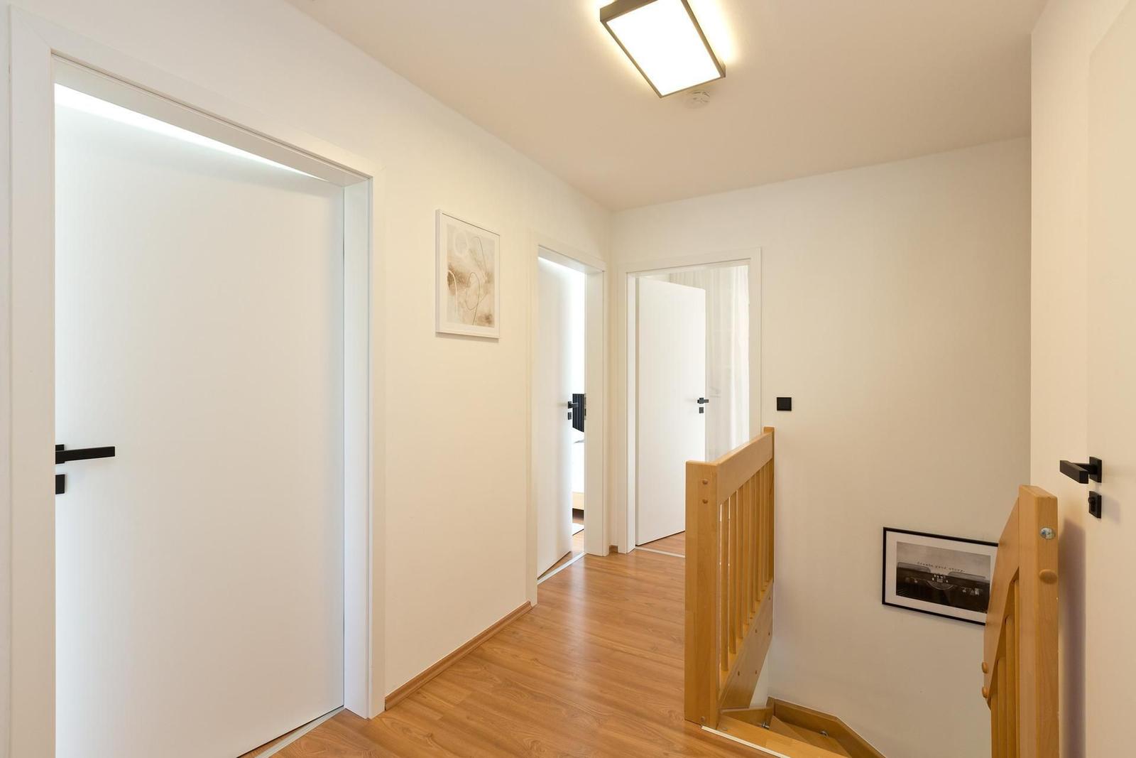 Flur mit Holzboden, weißen Türen und Holzgeländer. An der Wand hängen zwei Bilder.