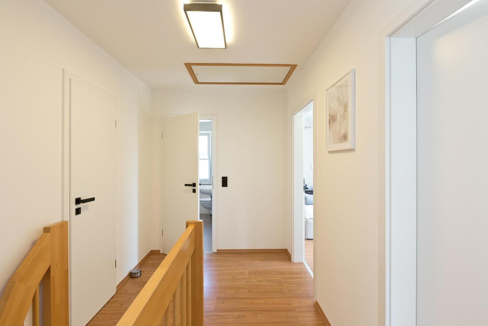Flur mit Holzboden, weißen Türen und moderner Deckenbeleuchtung. Blick in Schlaf- und Badezimmer.