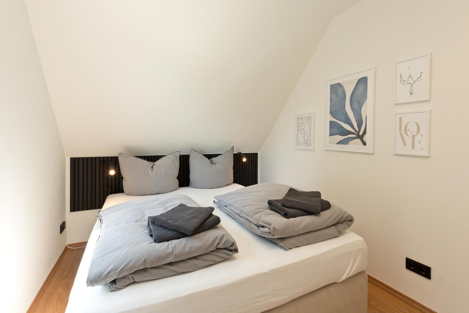 Schlafzimmer mit Doppelbett, grauen Kissen und Kunst an der Wand.