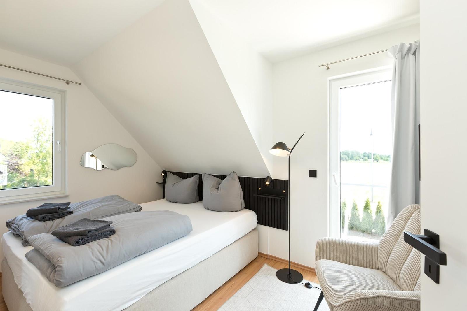 Schlafzimmer mit Dachschrägen, Bett, Sessel und Fenstern.