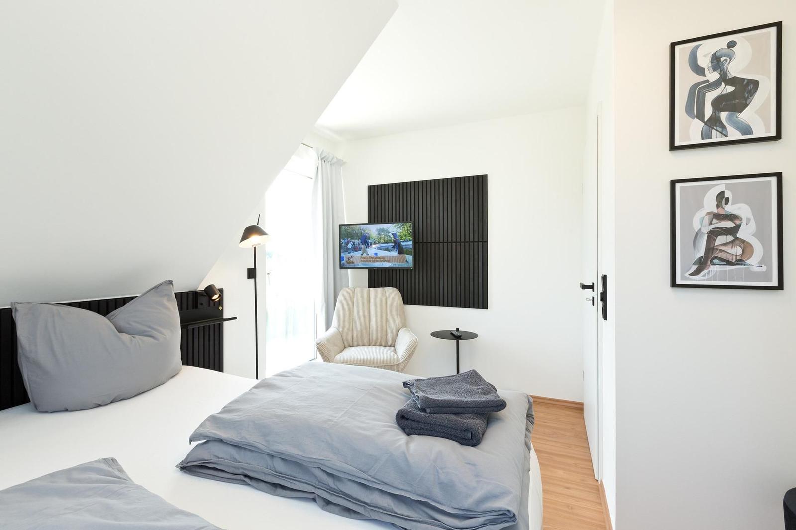Schlafzimmer mit Bett, Sessel, Fernseher und Wandbildern.