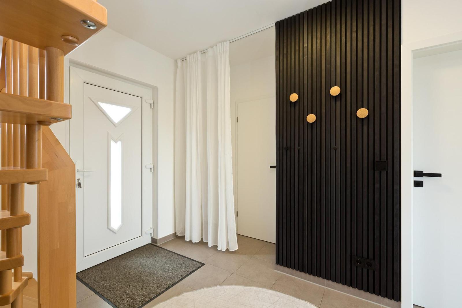 Eingangsbereich mit Holztreppe, weiße Tür und schwarze Holzwand mit runden Knöpfen.
