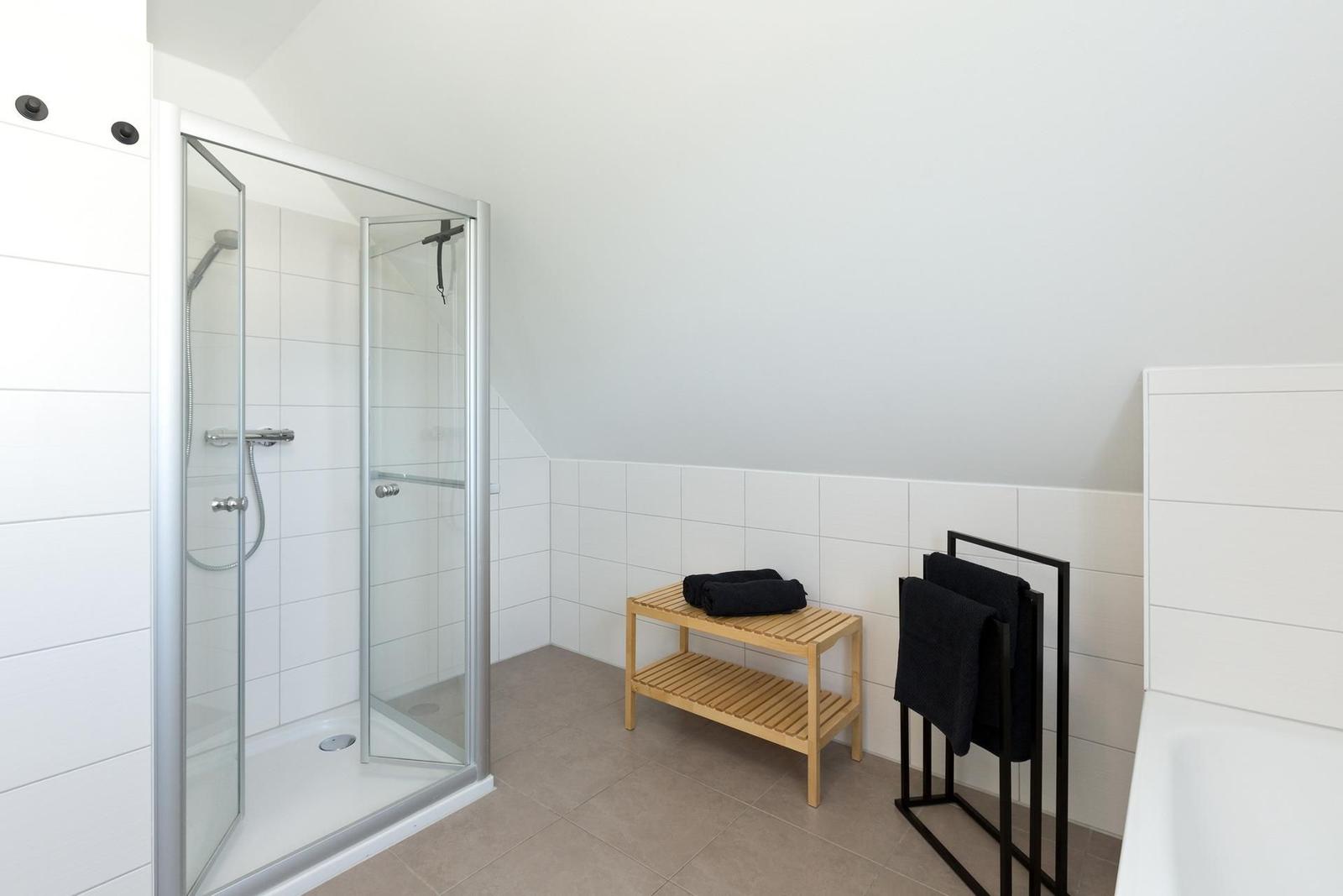 Dusche mit Glaswand, Holzbank und Handtuchhalter in weißer Umgebung.