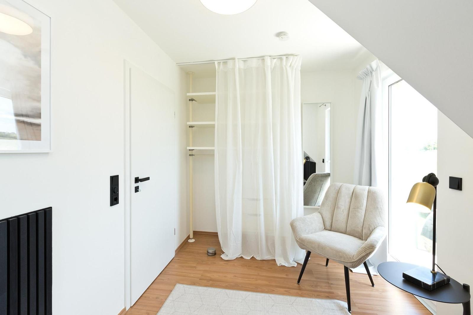 Schlafzimmer mit weißen Wänden, Holzboden und goldener Stehlampe.