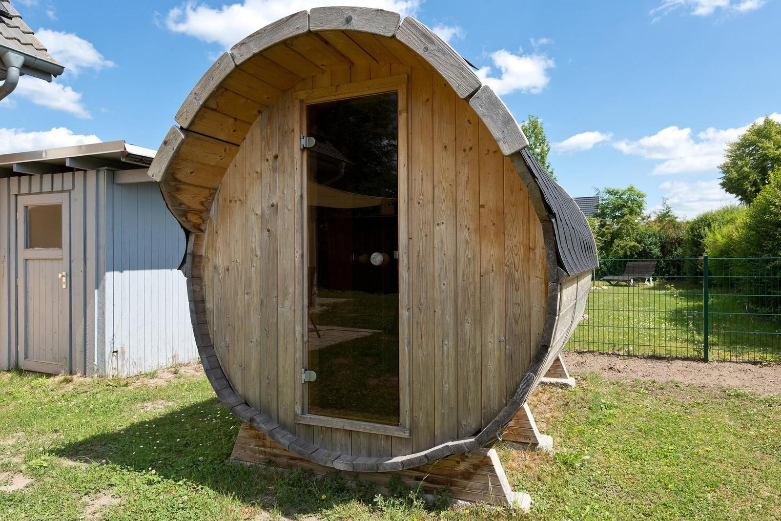 Holzsauna im Stil eines Fasses mit Glasschiebetür im Garten.