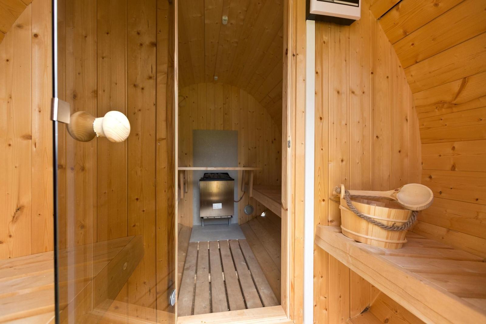Sauna mit Holzwand, Sitzbank und Holztonne mit Löffel